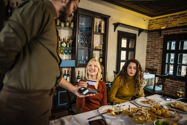 Photo of two female friends paying by credit card in restaurant after dinner